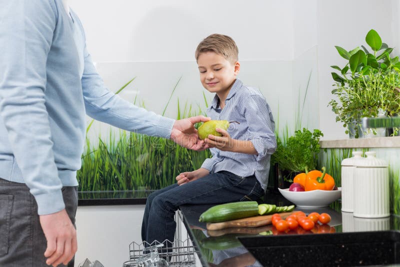 Midsection отца давая грушу к сыну в кухне стоковые фото